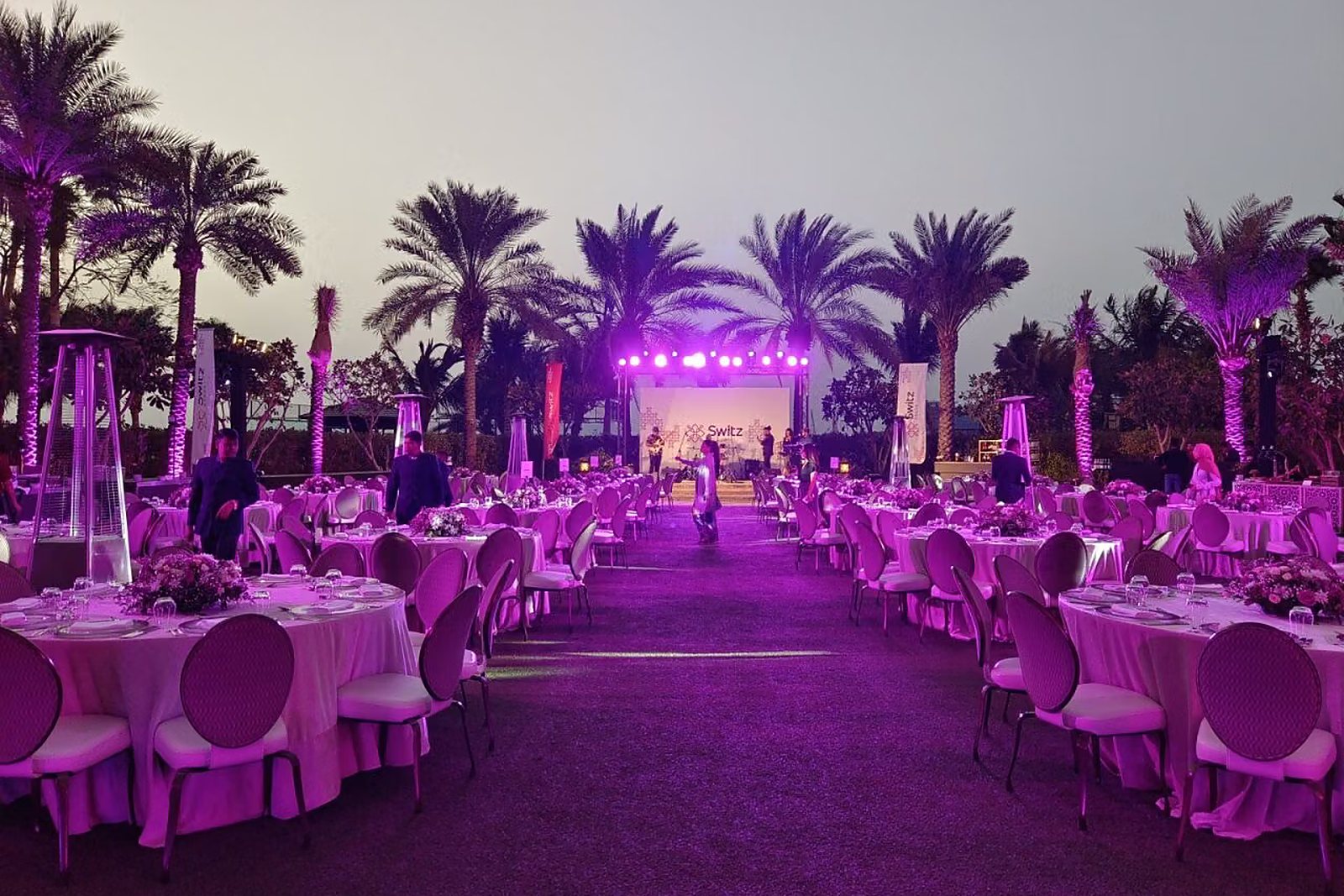Outdoor gala dinner among palm trees with purple uplighting