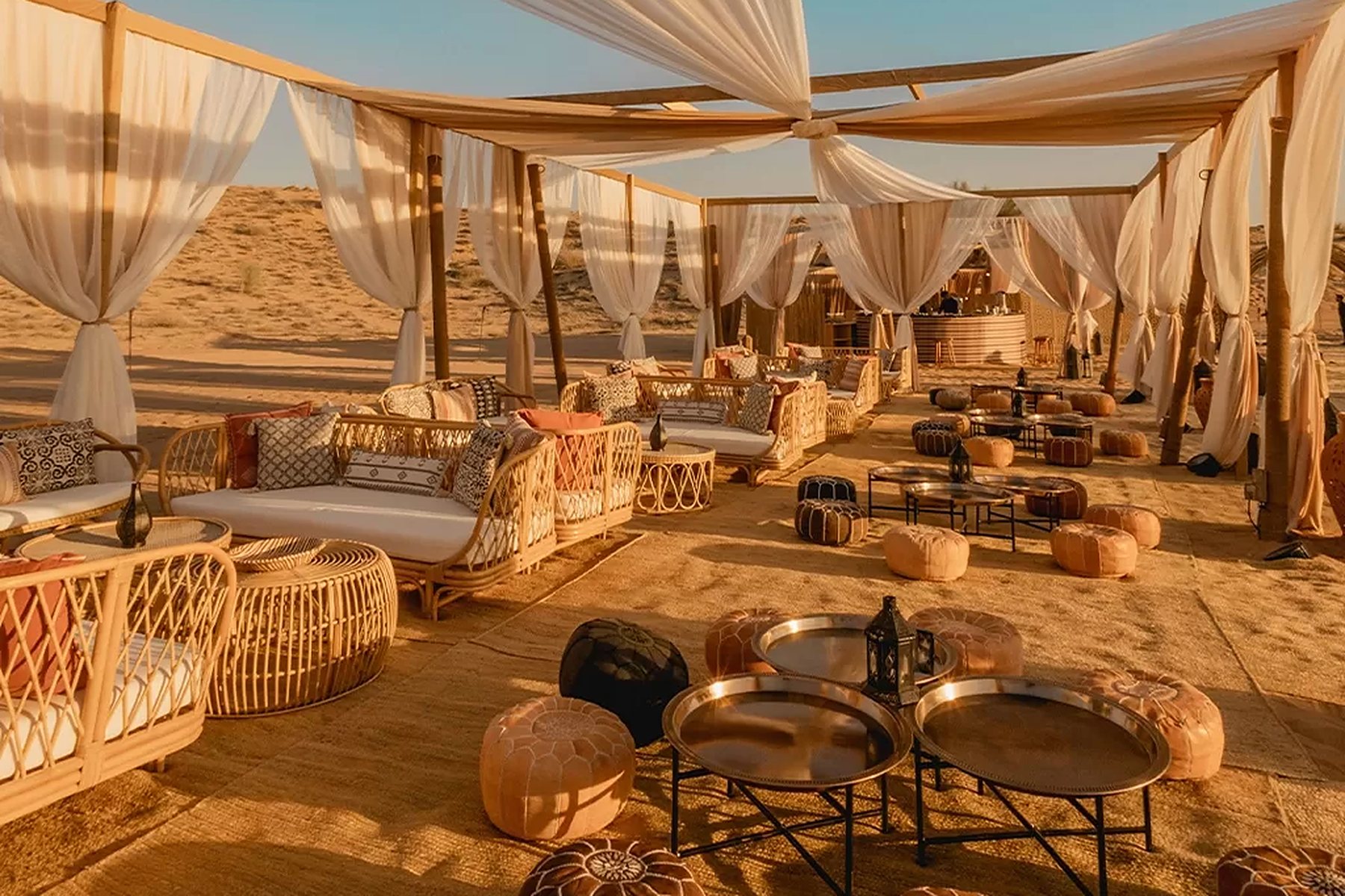 Desert camp lounge with white drapes, rattan seating and leather poufs